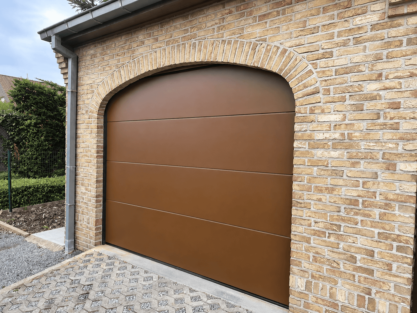 Bruine sectionale garagepoort in een gemetselde boogopening